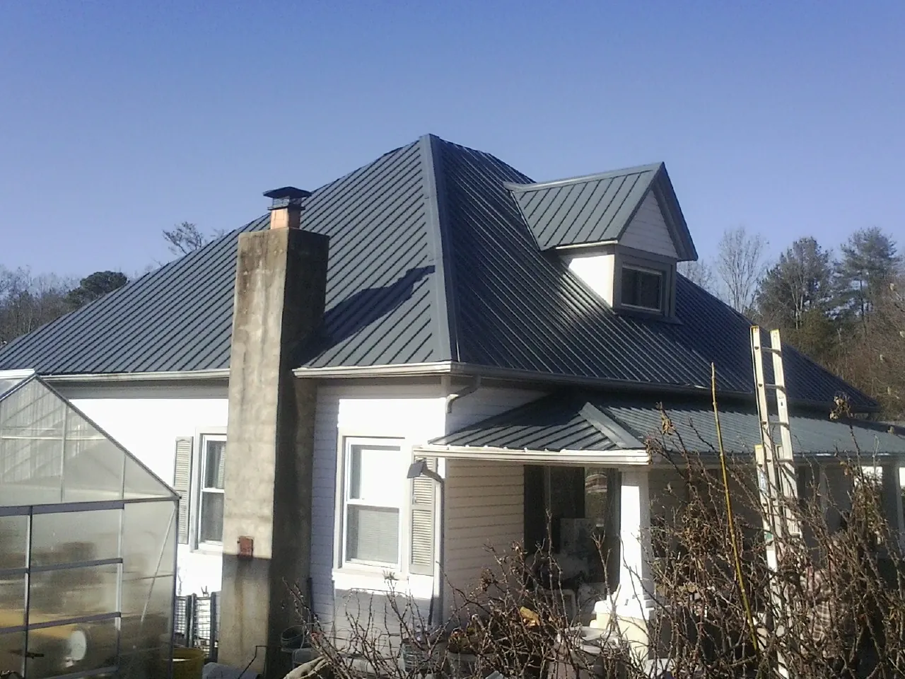 Dark blue standing seam metal roof on a white farmhouse with dormer — Slate & Tile Roof Repair by Roofing Brothers in Rockaway Park