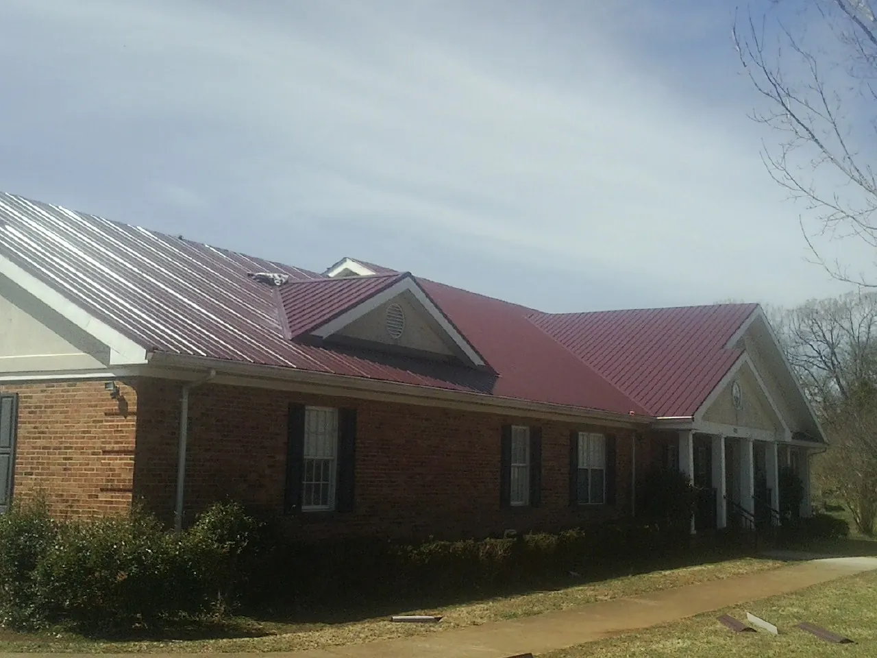 Red metal roof with gabled entries on a long brick building, from a Hail Damage Roof Repair job in Rockaway Park