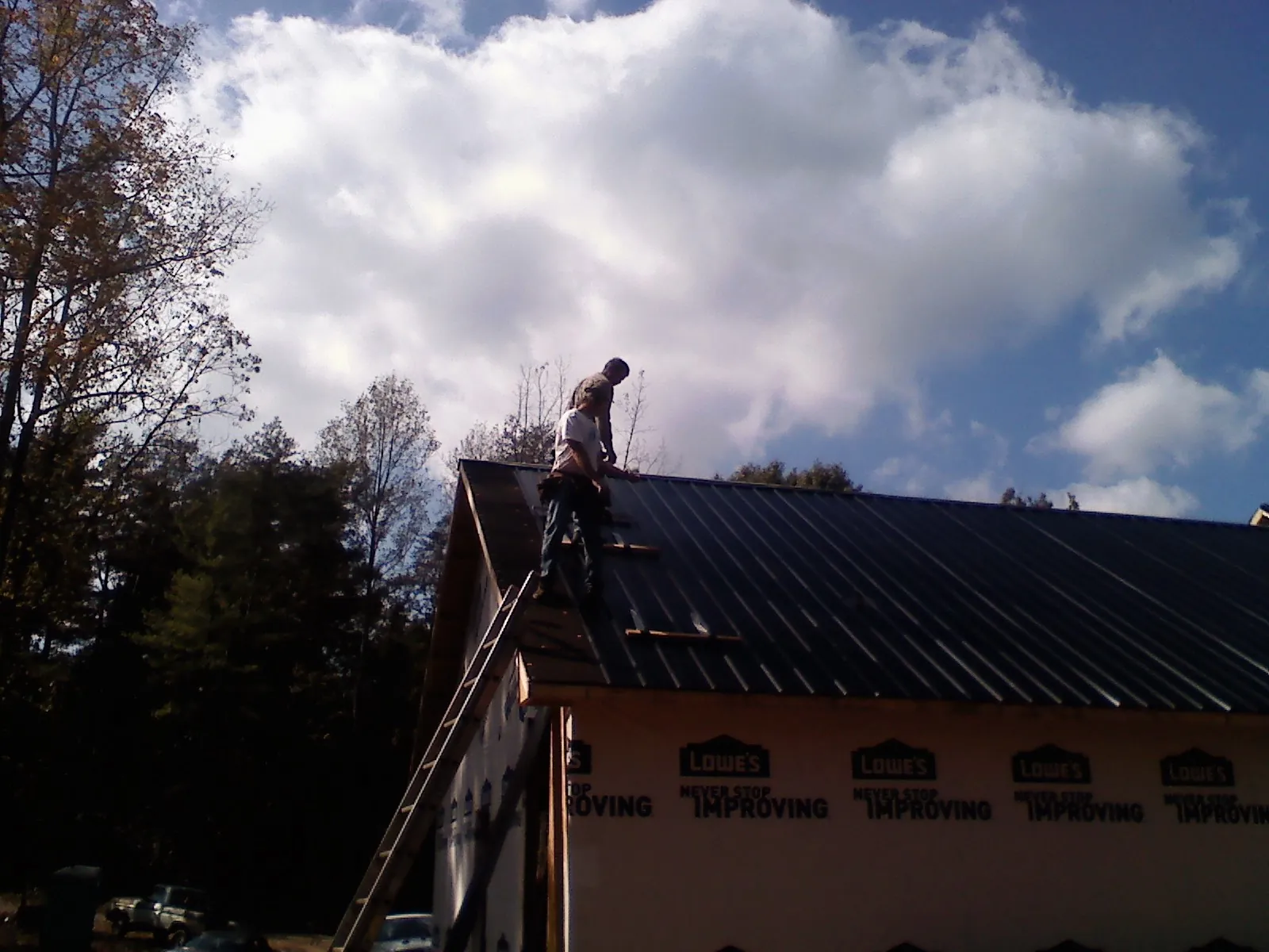 Roofer fastening dark metal panels high against a cloudy sky, from a Roof Inspection job in Rockaway Park