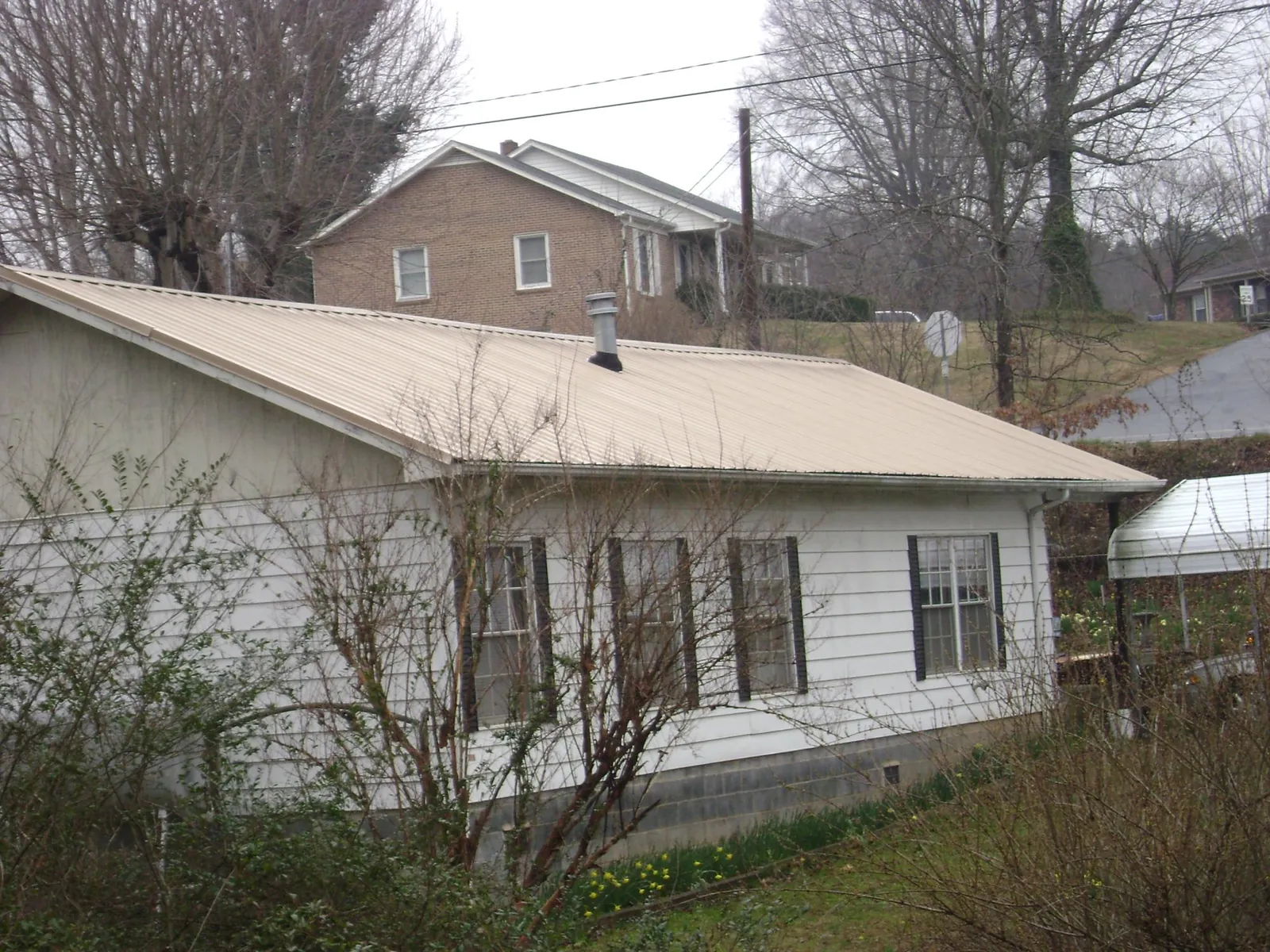 Tan metal roof on a white sided house set into a hillside — Commercial Roofing by Roofing Brothers in Rockaway Park